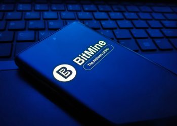 Closeup of a dark blue smartphone displaying the bitmine logo and text, resting on a laptop keyboard in a dimly lit, bluetoned environment , New York City, 15 December 2025
