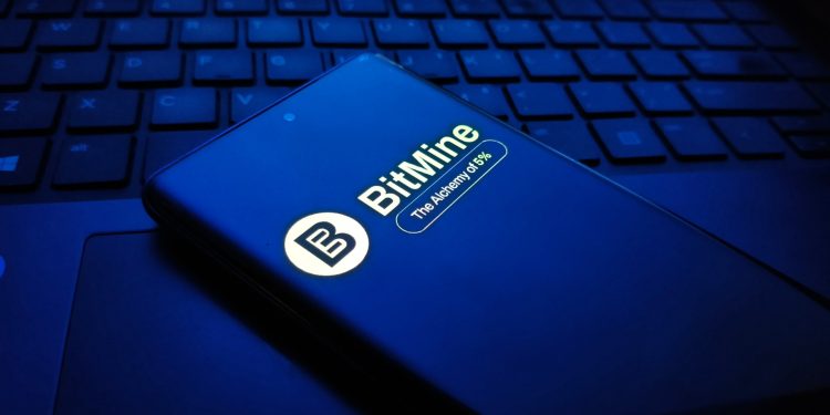 Closeup of a dark blue smartphone displaying the bitmine logo and text, resting on a laptop keyboard in a dimly lit, bluetoned environment , New York City, 15 December 2025