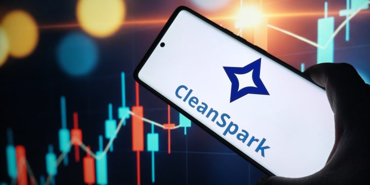 CleanSpark logo on smartphone screen with stock market chart background