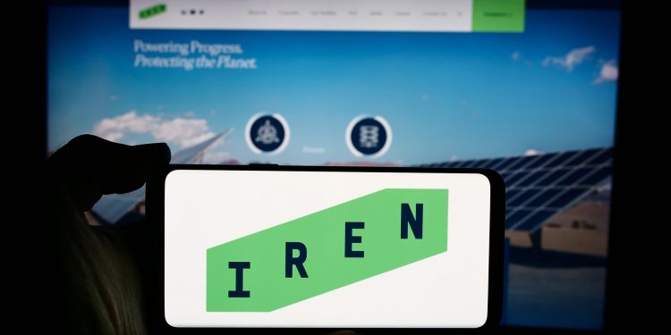 Bitcoin Rout Triggers After-Hours Bloodbath for Miners as IREN Misses Big缩略图 Person holding cellphone with logo of Australian Bitcoin mining company Iris Energy Ltd. (IREN) in front of webpage. Focus on phone display.