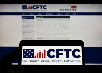 Person holding cellphone with logo of American Commodity Futures Trading Commission (CFTC) on screen in front of webpage. Focus on phone display.