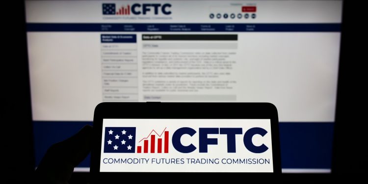 Person holding cellphone with logo of American Commodity Futures Trading Commission (CFTC) on screen in front of webpage. Focus on phone display.