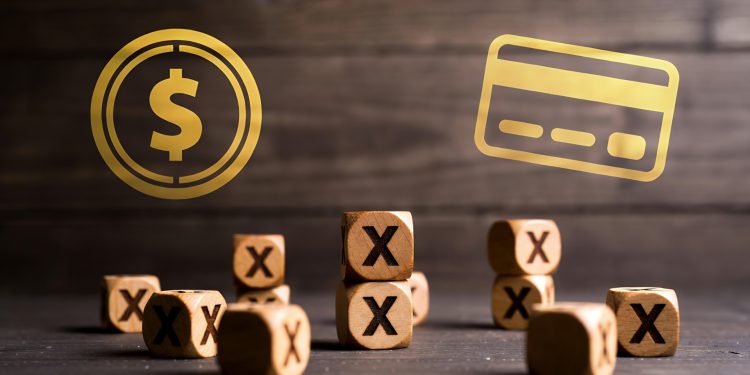 Numerous wooden blocks marked with "X" are scattered, while a dollar coin and credit card float above.