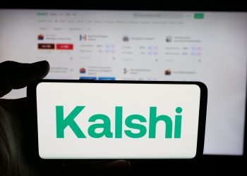 Person holding cellphone with logo of US prediction market company Kalshi Inc. on screen in front of webpage. Focus on phone display.