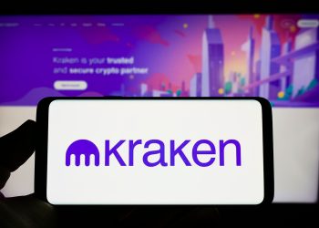 Stuttgart, Germany - 09-26-2022: Person holding mobile phone with logo of American crypto company Payward Inc. (Kraken) on screen in front of web page. Focus on phone display.